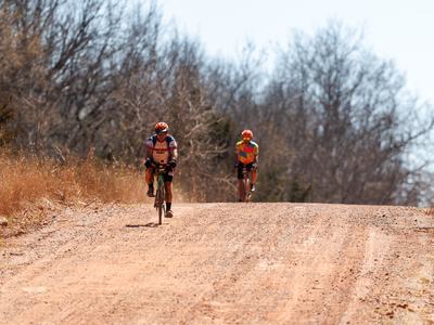 Two bikers race to finish on red dirt gravel roads in Oklahoma.