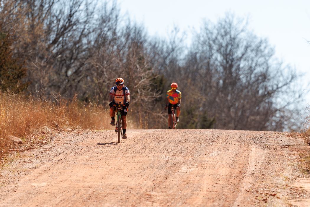 Two bikers race to finish on red dirt gravel roads in Oklahoma.
