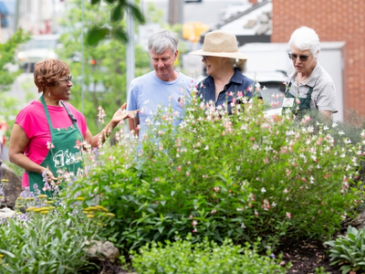 Two women in green Master Gardener aprons lead a tour through colorful gardens.