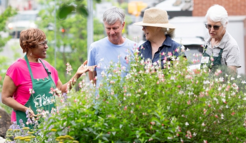 Two Master Gardener volunteers in green aprons lead a tour through colorful demonstration garden.