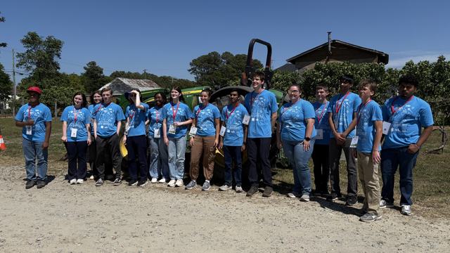 group of students in blue shirts posing for photo at farm