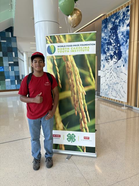 Teen 4-H Youth standing beside NC Youth Institute Banner