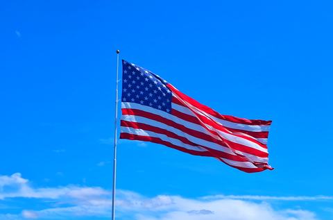 American flag waving from a tall flagpole against a vivid blue sky with wispy white clouds.