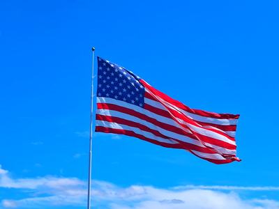 American flag waving from a tall flagpole against a vivid blue sky with wispy white clouds.