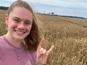 Female college student smiling and standing in a wheat field.