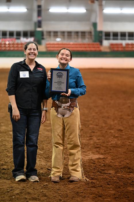 Junior Sportsmanship Winner Hallie Hardy and Extension Associate Alaina Cross are posing in the main arena with Hallie holding her plaque.