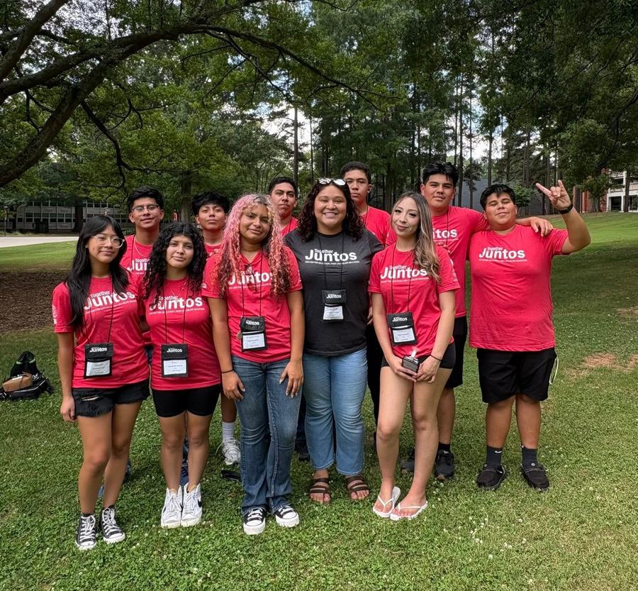 Pictured are 10 Juntos Members and Yuli, the Juntos Coordinator. They have matching Juntos shirts and are outside on NC State campus near Fountain Dining Hall.