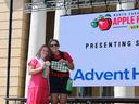 Two women stand side buy side on the Apple Festival Stage. One is wearing a pink dress and holding a prize ribbon. One is holding a gingham oven mitt. They are both smiling.