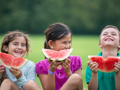 Three children eating watermelon outside on a summer day