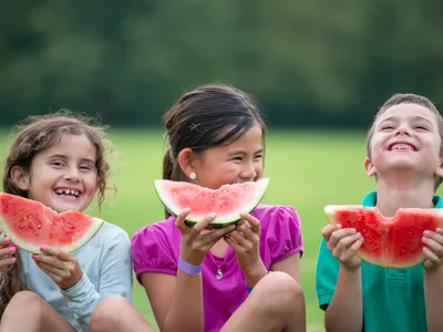 Three children eating watermelon outside on a summer day