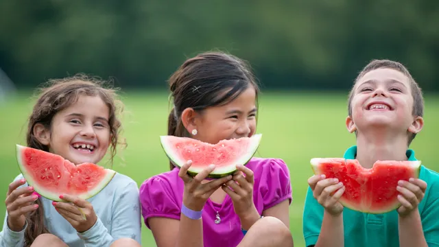 Three children eating watermelon outside on a summer day