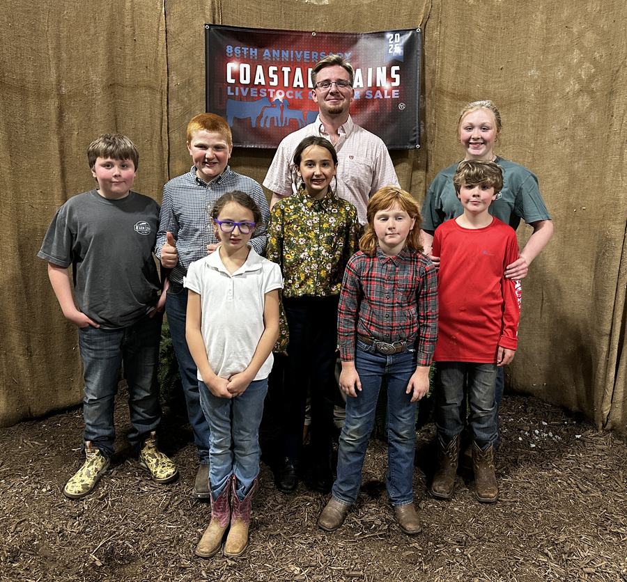 7 of the Craven County youth who showed in the 4-H Livestock Show and Sale standing together with the judge from the show in front of a banner that says "Coastal Plains Livestock Show and Sale"