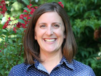 A profile photo of NC State Extension Interim Assistant Director of Youth Programs Liz Driscoll smiling, with flowering shrubbery in the background.