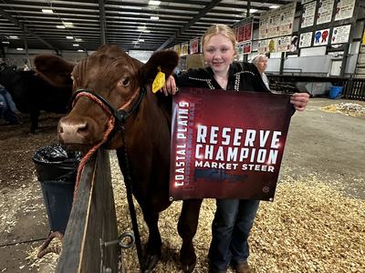 Craven County youth holding a banner beside her reserve champion market steer at the Coastal Plains Livestock Show and Sale 2026. The banner says "Reserve Champion Market Steer"