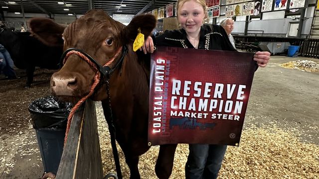 Craven County youth holding a banner beside her reserve champion market steer at the Coastal Plains Livestock Show and Sale 2026. The banner says "Reserve Champion Market Steer"