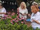 Three women holding clipboards look at purple and pink flowers