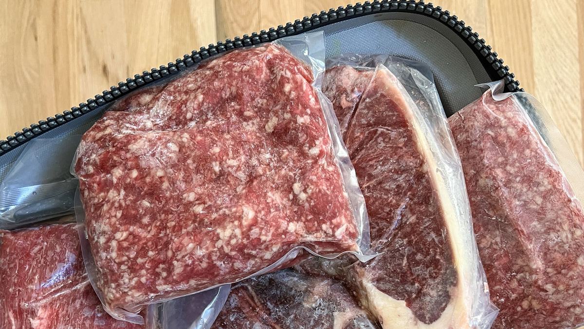 Sealed packs of ground beef are shown on a wooden table.