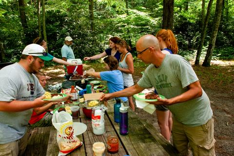 People serving themselves food around a picnic table outside