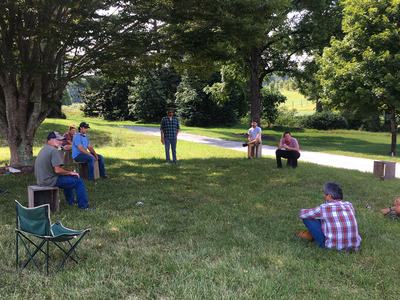 People sitting at socially-distanced intervals in grassy lawn