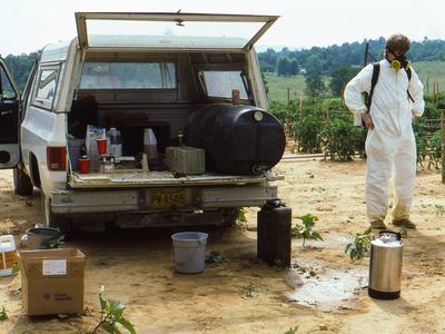 Person in spray suit with open pickup truck in field