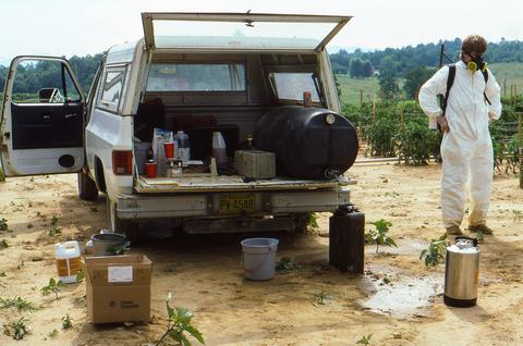 Person in spray suit beside pickup truck in field