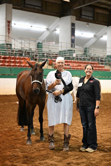Bill Crouse posing with his "Most Fly Alumni" challis alongside Alaina Cross. Bill is dressed in a hospital gown and arm sling and his holding his bay horse.