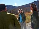 A man and two women are having a discussion with an agrarian scene in the background