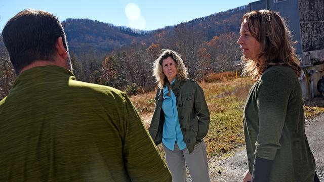A man and two women are having a discussion with an agrarian scene in the background