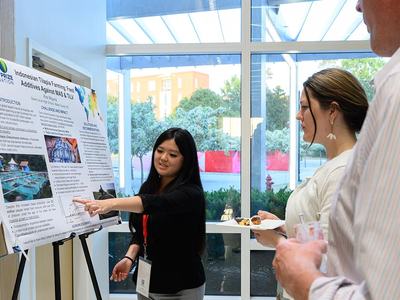 A North Carolina 4-H'er named Kira Wiguna points to a graph on her research poster