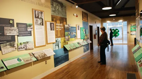 The inside of the 4-H History and Learning Center; informational panels and historic photos line the walls while two visitors read the displays.