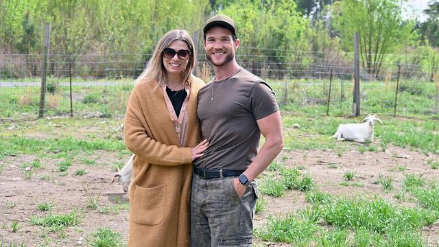 A husband and wife pose at a farm in Durham County with a goat in the background