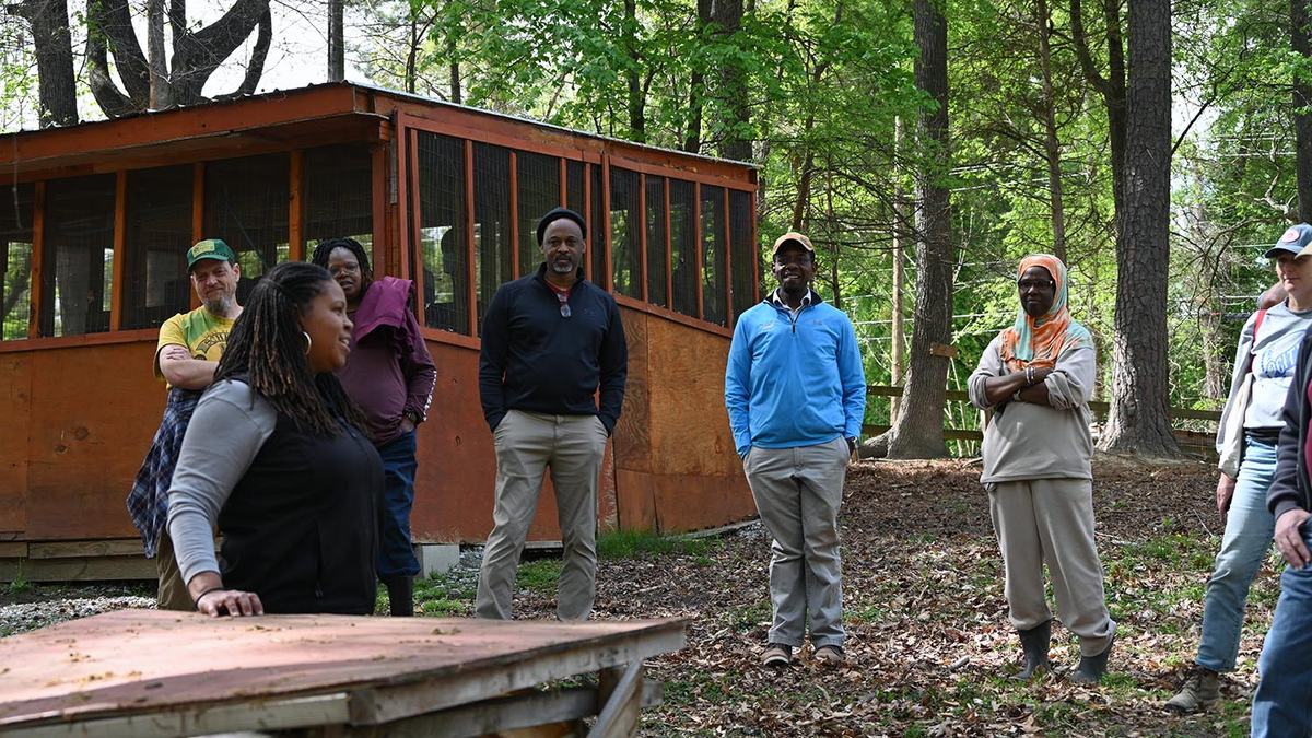 A female farmer stands next to a compost bin while explaining its use to onlooking visitors
