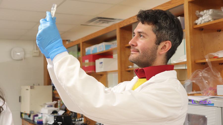 Orlando Arguello-Miranda, microbiologist at NC State's College of Agriculture and Life Sciences, in a lab coat examining Neo-P samples in the lab.