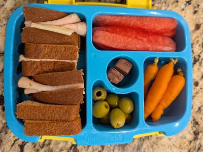 bento style lunch container with a sandwich, watermelon, carrots, and olives.