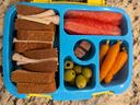 bento style lunch container with a sandwich, watermelon, carrots, and olives.