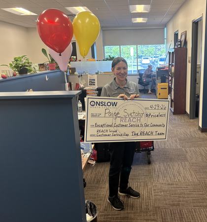 Paige holding a big sign that looks like a fake check and reads Exceptional Customer Service to our Community.