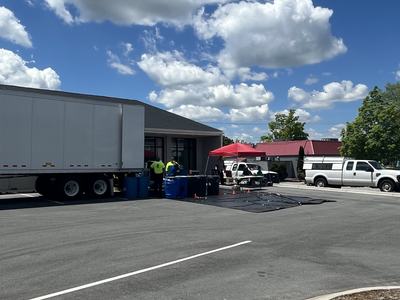 Parking lot set up for pesticide collection with tractor trailer, barrels and tarp covering parking lot.