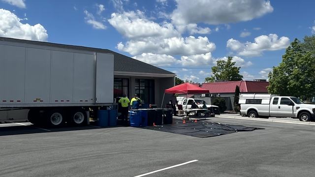 Parking lot set up for pesticide collection with tractor trailer, barrels and tarp covering parking lot.