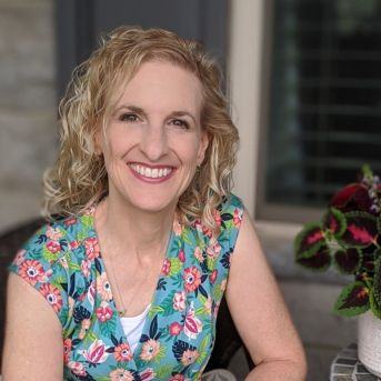 Phyllis Knight smiling and sitting on a porch next to a coleus plant.