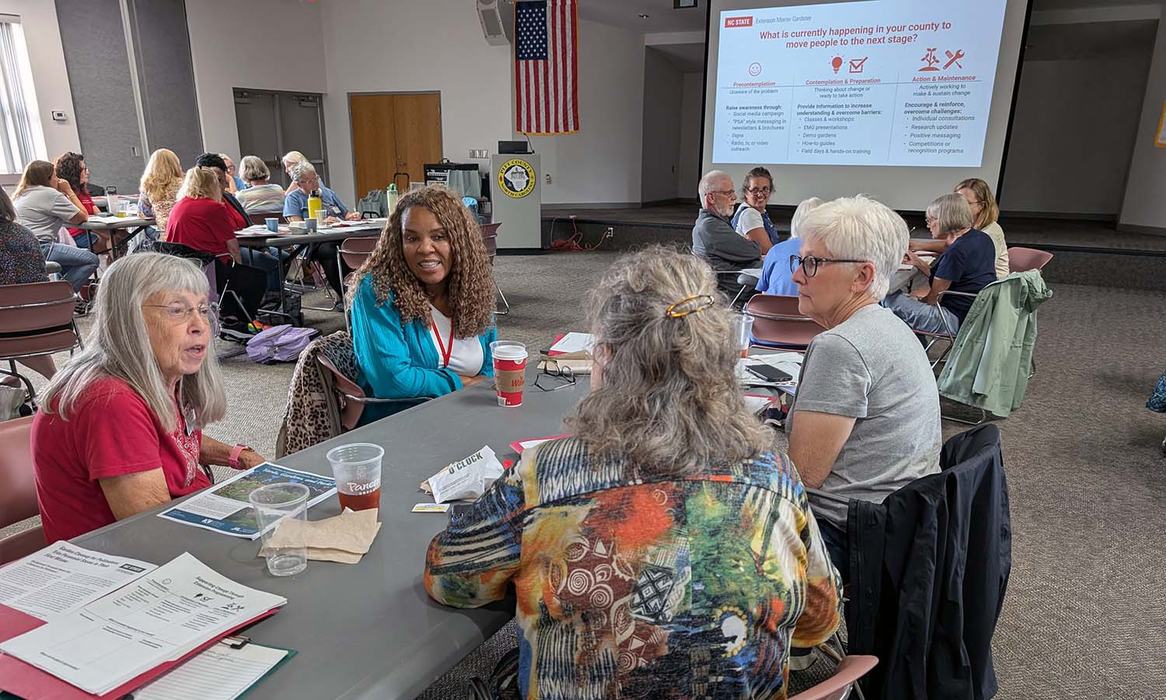 Four women talk while sitting at a table in a classroom