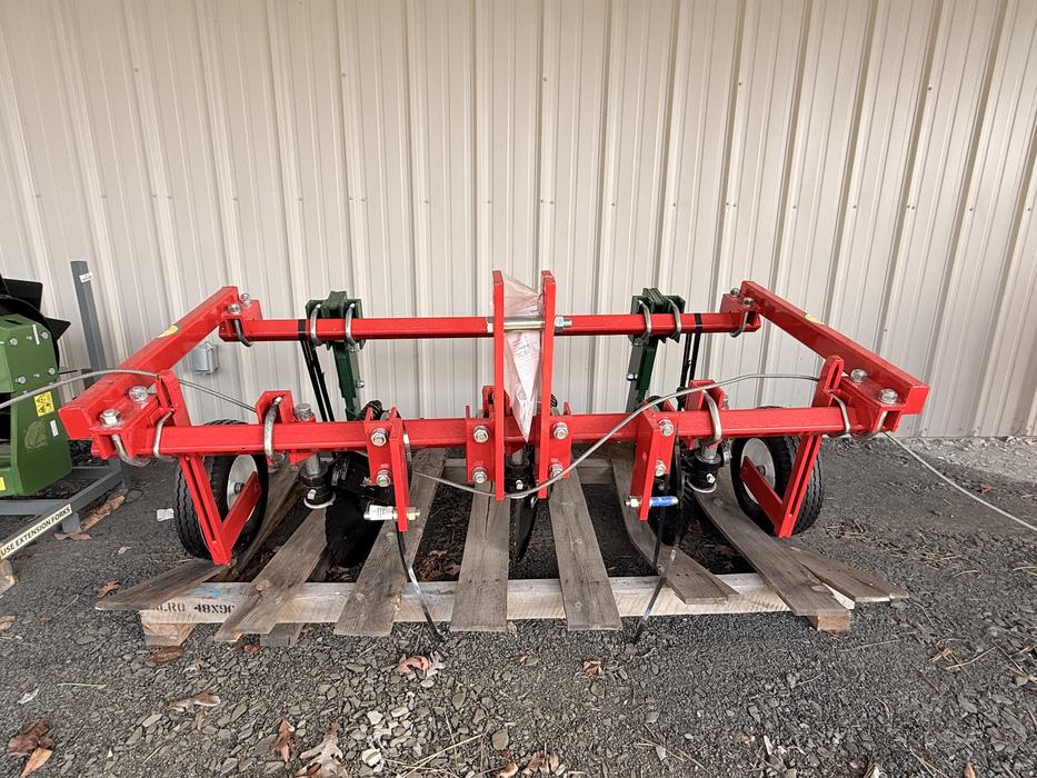 A red agricultural implement, specifically a plastic lifter or ripper, sits on a wooden pallet.