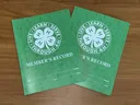 Two green 4-H project record books with white 4-H emblems and the motto "Live • Learn • Serve • Through 4-H" overlap on a wooden table.