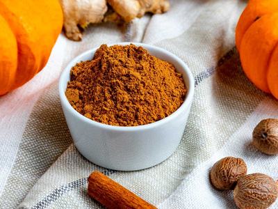 Small dish of a reddish brown powdery spice are surrounded by ingredients like cinnamon and ginger as well as decorative pumpkins.