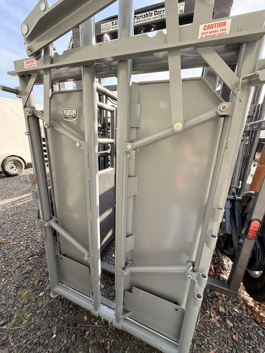 A close-up of a heavy-duty, gray metal Pearson Livestock Equipment head gate, part of a Rawhide portable corral system.