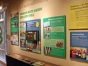 Interior exhibit featuring historical photographs, informational panels and memorabilia highlighting North Carolina 4-H awards, scholarships, competitions and national recognition. A glass display case holds ribbons, medals and other artifacts, with a sta