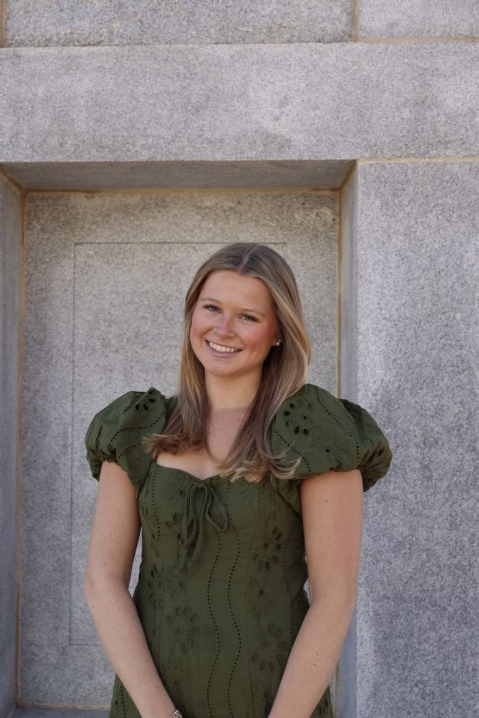 Young woman poses in green dress in front of cement background.