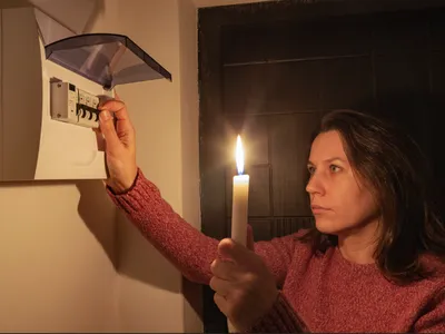 Lady checking electric box while holding candle in dark.