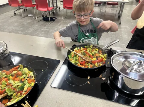 A young child cooks a vegetable stir fry in a 4-H apron