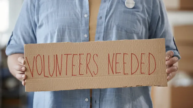 Image of person holding a sign that says Volunteers Needed