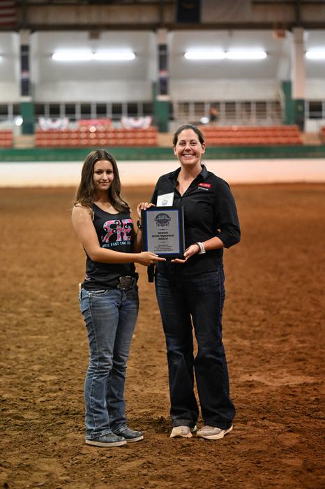 Senior Sportsmanship Winner Abigail Poirrier and Extension Associate Alaina Cross are posing in the main arena with Abigail holding her plaque.